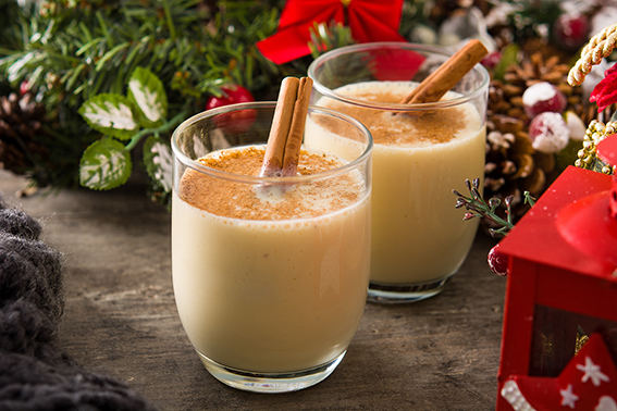 Homemade eggnog with cinnamon in glass on wooden table. Typical